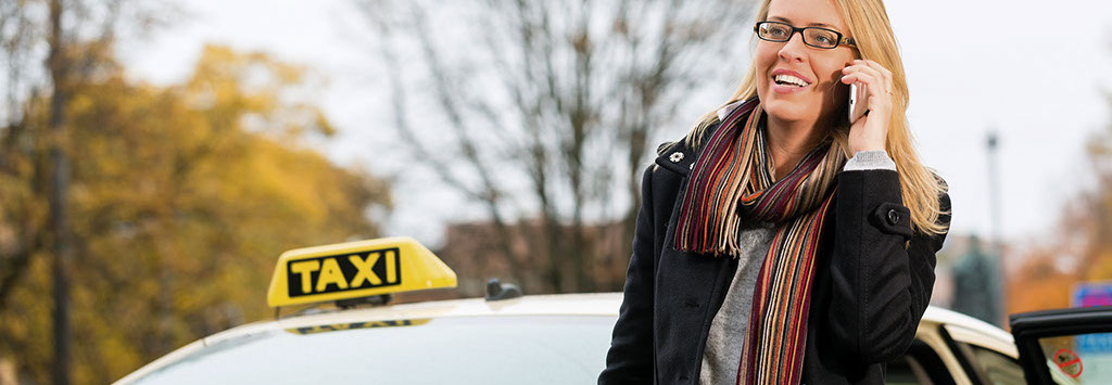 Frau mit Mobiltelefon steht beim Taxi